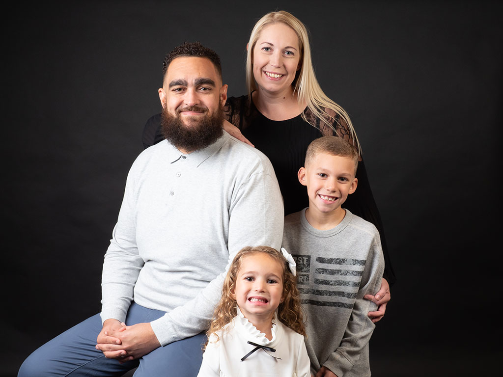 happy family of four against black background taken by family photographer in Braintree